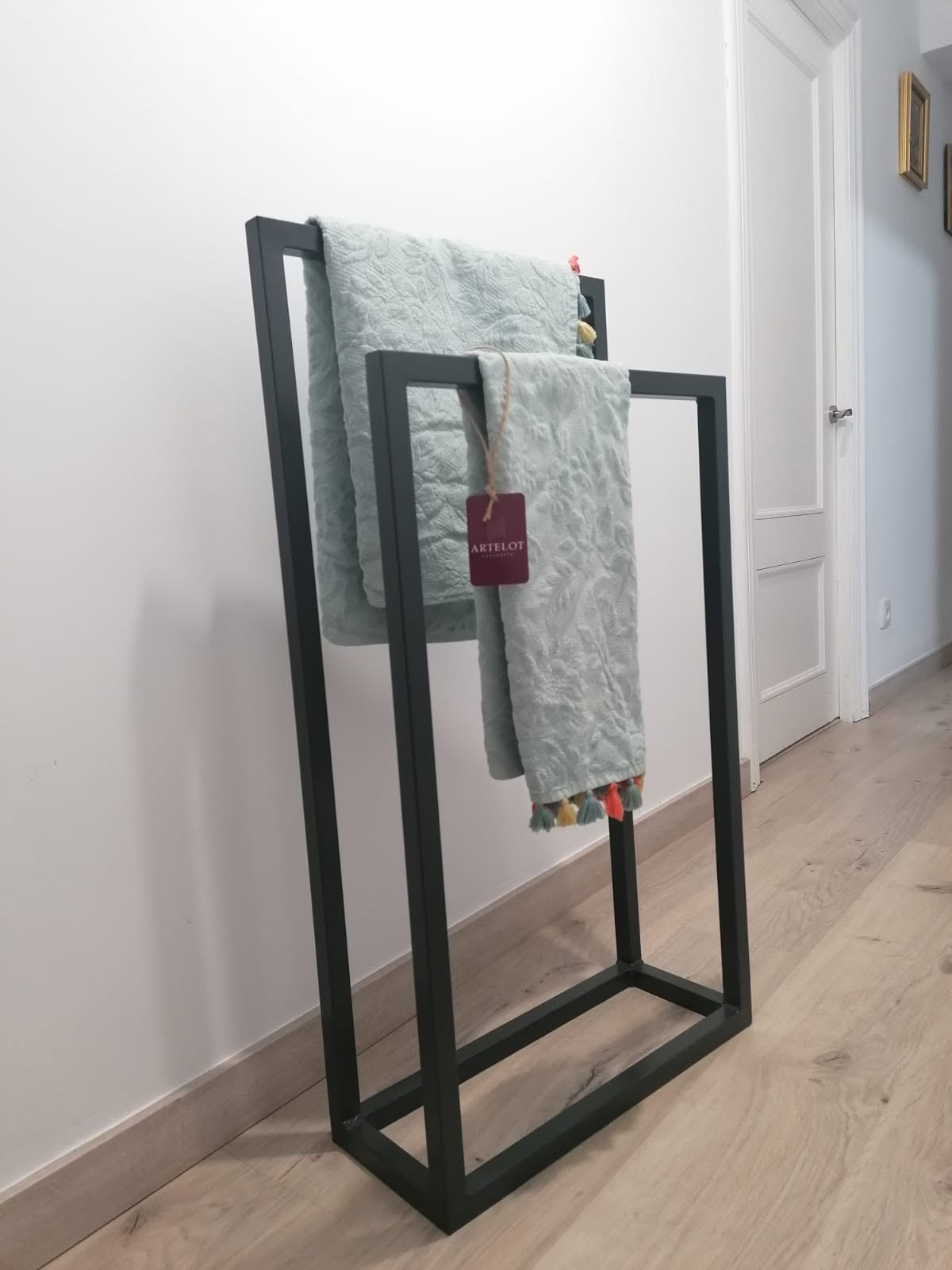 Toallero Galán Artelot de acero negro instalado junto a un baño